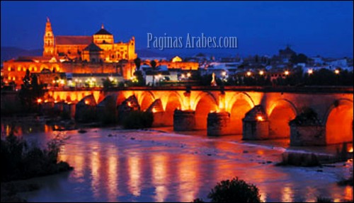 Córdoba, bañada por el río Guadalquivir, al anochecer, con la Mezquita y la catedral al fondo.